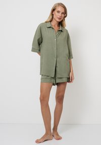 Camisa de botones de manga corta en verde olivo combinada con pantalones cortos a juego. Tejido texturizado con un patrón sutil, corte relajado, sin acentos visibles.