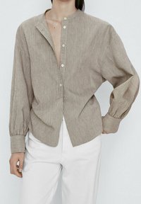 Chemise à rayures beige et crème, boutonnée, avec col montant, coupe ample et manches longues à poignets froncés. Texture de tissu lisse.