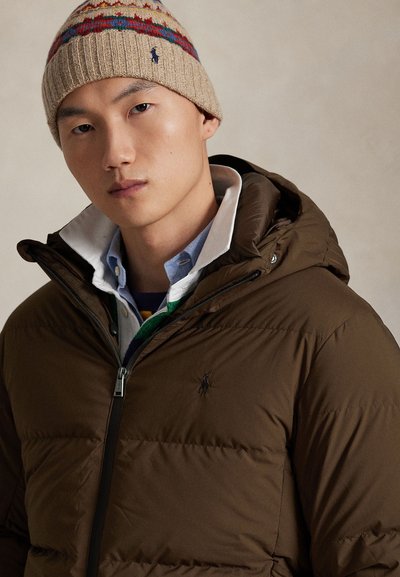 Brown puffer jacket with a zippered front and hood, accented by a logo. Paired with a blue collared shirt and a multicolored knit beanie.