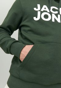 Green cotton hoodie featuring a large white logo, front pocket, ribbed cuffs and hem, with drawstring hood and smooth texture.