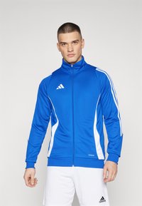 Kék sportdzseki magas gallérral, fehér csíkokkal �és cipzárral. Az Adidas logója a bal mellen található. Simább textúra.