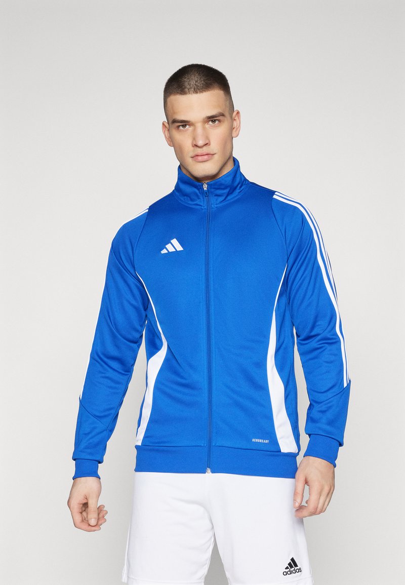 Kék sportdzseki magas gallérral, fehér csíkokkal és cipzárral. Az Adidas logója a bal mellen található. Simább textúra.
