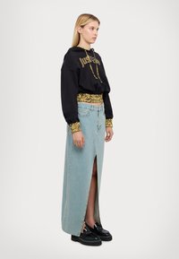 Felpa nera corta con scritte dorate, abbinata a una gonna maxi in jeans light blue con uno spacco alto. Scarpe con plateau nere completano il look.