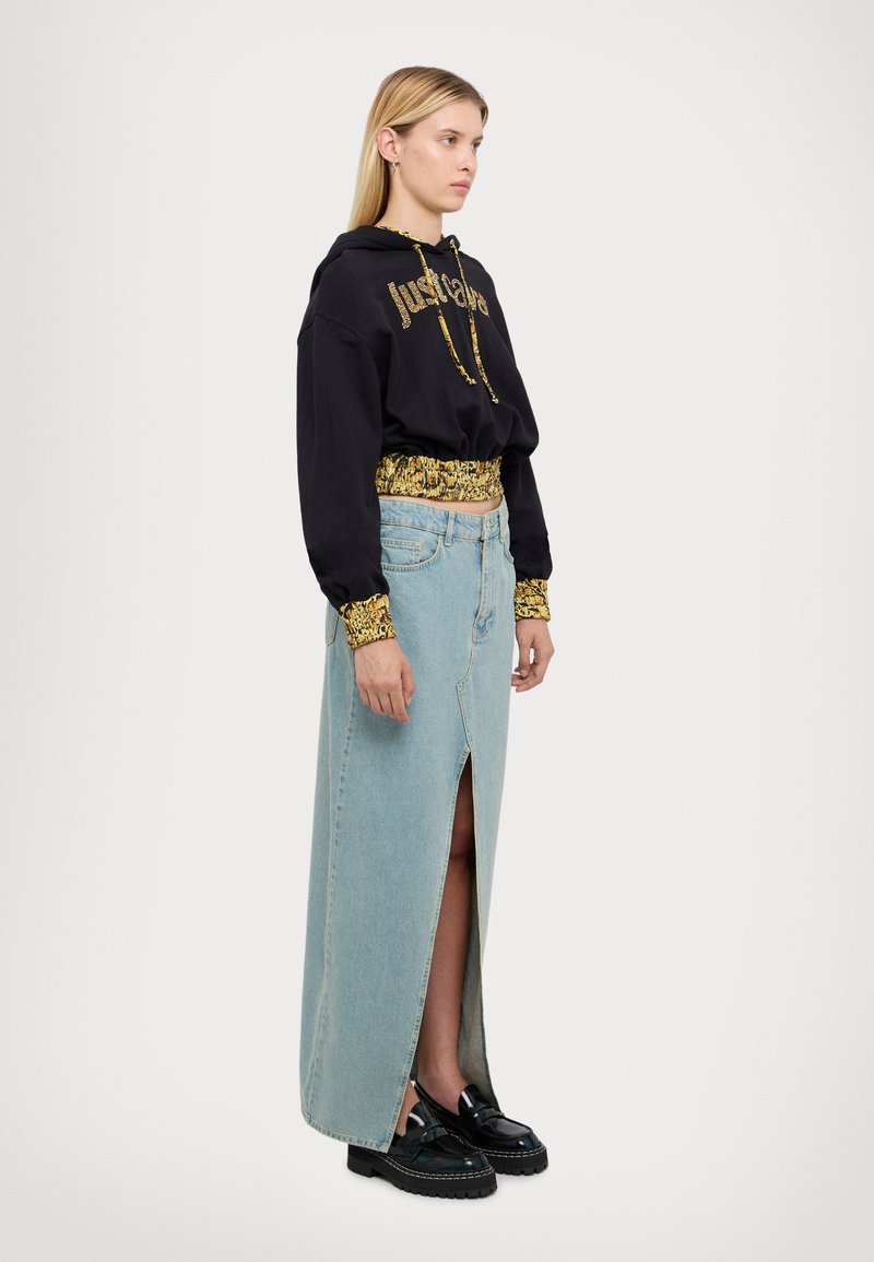 Felpa nera corta con scritte dorate, abbinata a una gonna maxi in jeans light blue con uno spacco alto. Scarpe con plateau nere completano il look.