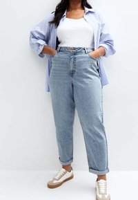 Světlé modré džíny s vysokým pasem a volným střihem, s ohrnutým lemem, doplněné bílým tílkem a modrou pruhovanou oversized košilí. Hnědé tenisky.