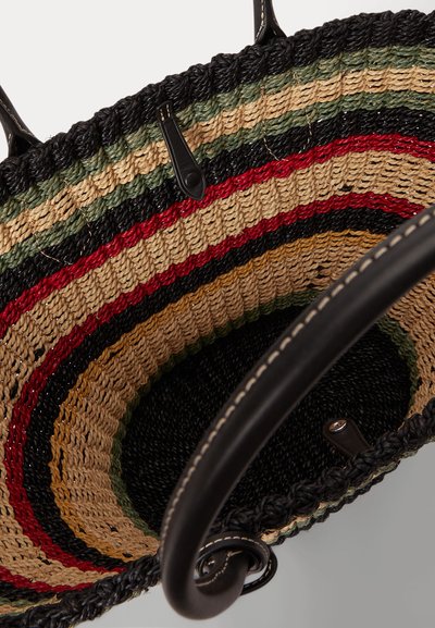 Κλείσιμο εσωτερικού υφασμάτινης τσάντας με συγκεντρικές ρίγες σε μαύρο, κόκκινο, μπεζ, πράσινο και φυσικές ίνες, με μαύρες δερμάτινες λαβές.