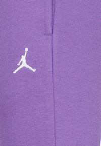 Pantaloni da jogging viola in cotone, con il logo Jordan bianco sulla coscia. Il tessuto ha una superficie liscia e una vestibilità comoda.