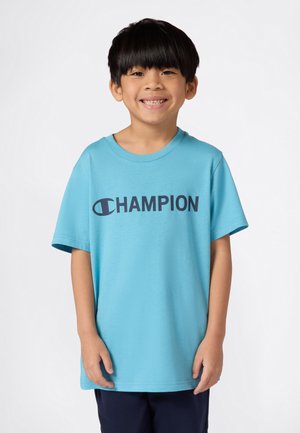 Maglietta in cotone azzurro chiaro con un grande logo navy "CHAMPION" sulla parte anteriore. Maniche corte e scollatura a girocollo offrono una vestibilità comoda.