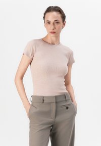 Light pink fitted short-sleeve top with ribbed texture, paired with high-waisted, tailored light brown trousers featuring a side pocket and button detail.