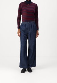 Haut à col roulé rayé bleu marine et rouge, associé à un pantalon large en denim foncé et ample ainsi qu'à des chaussures noires. Tenue décontractée avec ceinture élastique.