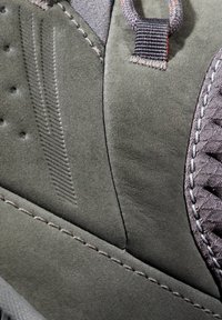 Chaussure gris foncé en matériau suédé, avec des coutures distinctes et des accents texturés. Présente des surfaces lisses et à motifs avec des coutures superposées.