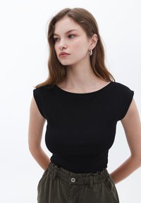 Svart ribbad t-shirt med kort ärm, figurnära design och rund halsringning, tillsammans med olivgröna högmidjade byxor med elastisk midja.