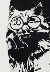 Μαύρη και άσπρη γάτα με στρογγυλά γυαλιά και να κρατάει έναν πίπα, απεικονισμένη σε μια λεπτομερή σχεδίαση πλεκτού υφάσματος.