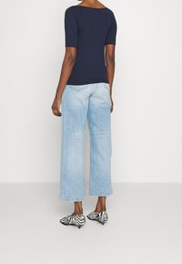 Námořnické tričko s krátkým rukávem, světle modré široké džíny a černo-bílé boty se zebřím vzorem. Zadní pohled zdůrazňuje ležérní styl.