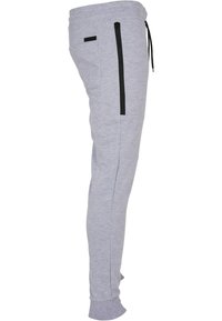 Pantalons de survêtement gris clair en tissu doux, présentant un design fuselé, une poche zippée sur le côté, des accents noirs et une taille élastique.