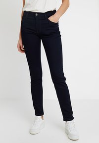 Granatowe wąskie dżinsy wykonane z denimu, z zamkiem błyskawicznym, przednimi kieszeniami i kontrastowym przeszyciem. W parze z białymi trampkami.