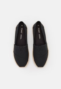 Scarpe slip-on nere in tela con superficie texturizzata e suole in juta intrecciata, caratterizzate da un design a V nella parte anteriore e morbida fodera interna.
