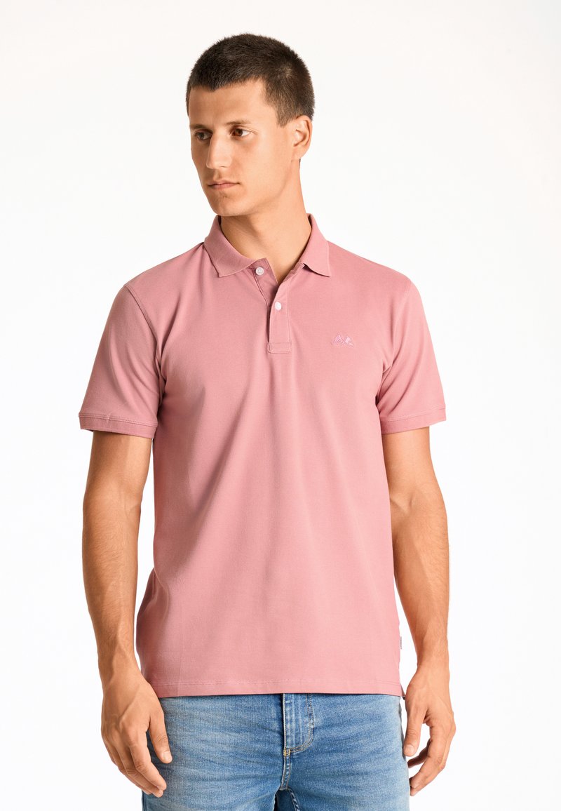 Polo shirt rosa in cotone con collo a polo, maniche corte e un sottile dettaglio del logo sul lato sinistro del petto. Indossato con jeans blu.