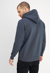 Felpa con cappuccio grigio scuro, maniche lunghe, polsini e vita a costine. Tessuto morbido con una vestibilità rilassata.