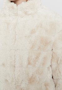 Krämfärgad, överdragsjacka i plysch med mjuk textur, med ett quiltat mönster, rundad krage och subtila beige detaljer.