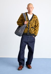 Leopardmønstret, fuzzy cardigan i gul og sort; parret med løse, mørkeblå denimbukser og brune fodtøj. Grå totebag.