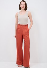 Beige ribbed tank top paired with high-waisted, wide-leg rust-orange trousers, featuring side pockets and a matching belt.