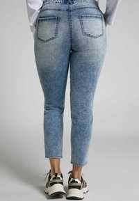 Ljusblå denimjeans med slim fit, kort längd, fransad fåll och två bakfickor. Bärs med svarta och beige sneakers.