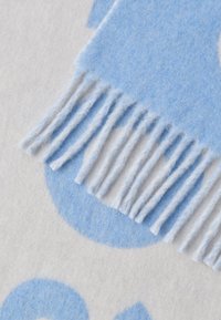 Jasnoniebiesko-szary tkany szal o miękkiej fakturze, z frędzlami na krawędziach i dużymi okrągłymi wzorami w różnych odcieniach niebieskiego.