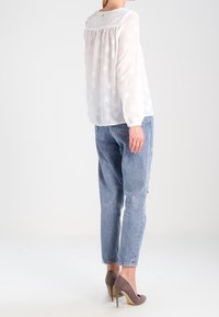 Blusa bianca a maniche lunghe con motivo a stelle, dalla vestibilità ampia. Abbinata a jeans chiari strappati e tacchi alti grigi.