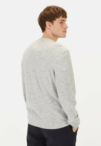 Grau gestrickter Pullover mit einem strukturierten Streifenmuster, Rundhalsausschnitt und gerippten Bündchen. Modell von hinten gezeigt, kombiniert mit dunklen Hosen.