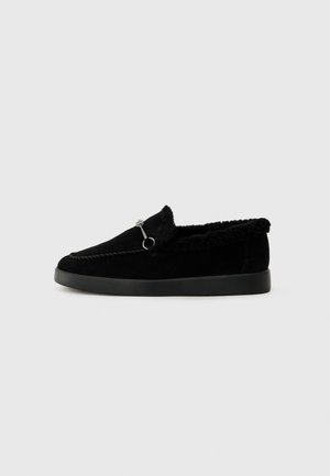 Sapatos pretos sem atacadores com um cabedal em camurça, forro em pelúcia sintética e um design minimalista. Apresenta costuras decorativas e um acabamento metálico.