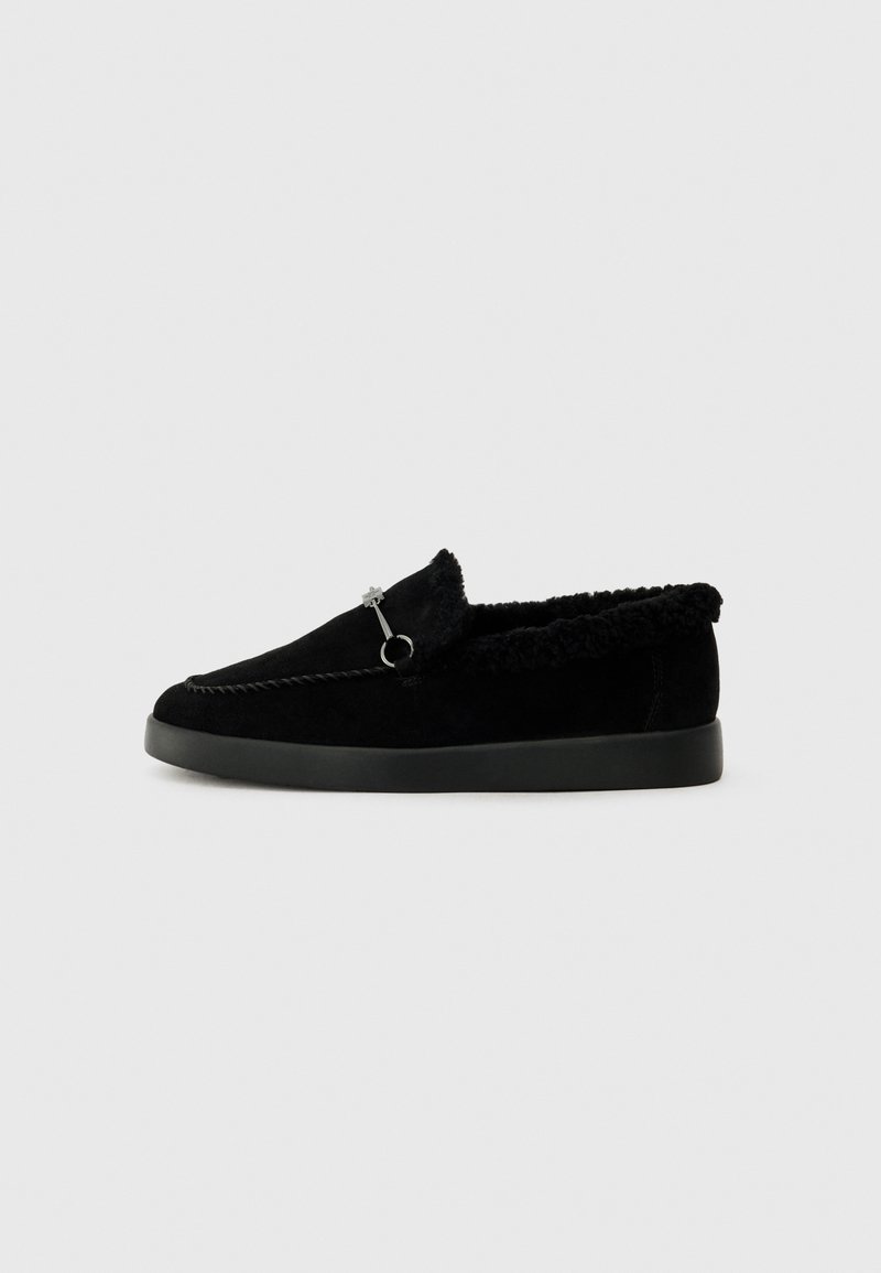 Sorte slip-on sko med overdel i semsket skinn, faux pelsfôr og minimalistisk design. Har dekorativ søm og en metalldetalj.