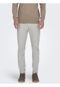 Suéter marrón combinado con pantalones gris claro. Los pantalones tienen un diseño de corte ajustado con una textura de tela suave. Zapatos marrones completan el conjunto.