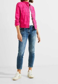 Fuchsia denim jacket with a collar, front buttons, and two chest pockets. Paired with light blue jeans and white sneakers.