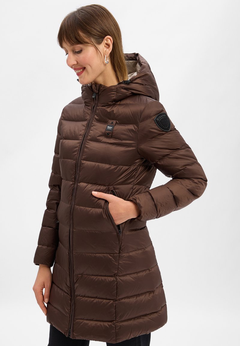 Bruine pufferjas met kap, met een horizontaal doorgestikte ontwerp, ritszakken en stoffen patches op de schouders. Soepele textuur.