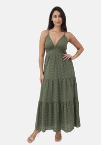 Abito lungo verde oliva con profondo scollo a V, spalline regolabili, orlo a balze con strati, e tessuto testurizzato con sottili accenti neri.