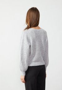 Gray ribbed knit sweater with balloon sleeves, cropped length, and raw hem. Worn over black trousers, soft texture visible.