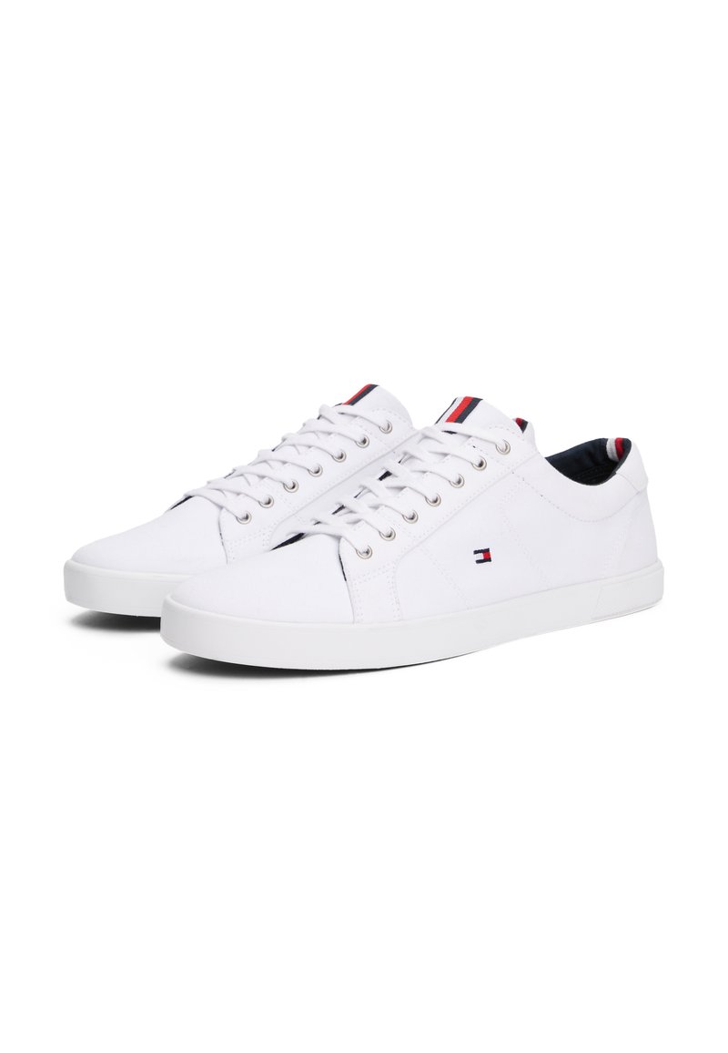 Zapatillas de lona blancas con un diseño de caña baja, que cuentan con cierre de cordones, suela de goma y un pequeño detalle de logo en el lateral.