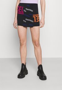 Zwarte mini-jurk met verschillende logo's in roze, paars en oranje. De stof is glad met een gestroomlijnde snit, gecombineerd met stevige zwarte enkelboots.