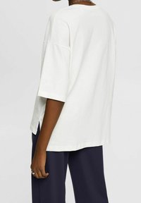 Camiseta blanca de gran tamaño hecha de algodón suave con mangas cortas, con aberturas laterales, combinada con pantalones sueltos de color marino.
