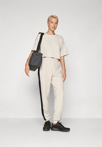 Svetlo bež kratka srajca in ujemajoče se hlače z ožanim krojem ter črnim stranskim trakom. Model nosi pravokotno črno torbico in črne superge.