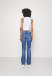 Top corto blanco combinado con jeans de campana azules. Los jeans tienen bolsillos traseros y un lavado de denim claro con un dobladillo deshilachado. Zapatillas blancas completan el look.