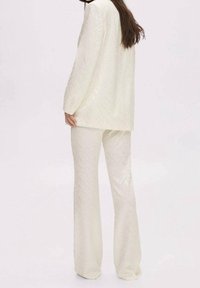 Kremowy dwuczęściowy zestaw składający się z długiego płaszcza i luźnych spodni, ozdobiony subtelnym wzorem w zygzak.