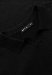 Polo nero in tessuto morbido, con colletto piatto e patta frontale, con un'etichetta che mostra "ombre" e taglia M.