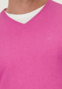 Roze v-hals trui van zacht materiaal. Heeft een geribbeld halslijn en subtiele logodetail, nauwsluitend ontwerp met een effen kleur.