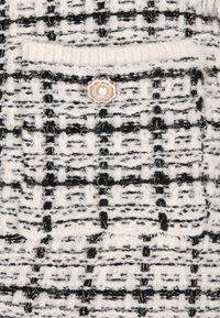 Fekete-fehér tweed szövet, textúrált rácsos mintával, kicsi zsebbel és gyöngyszerű gomb díszítéssel.