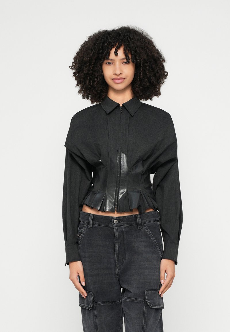 Schwarze, kurze Jacke mit einer glatten, glänzenden Vorderseite aus Kunstleder und strukturierten Ärmeln aus Stoff. Verfügt über einen verdeckten Reißverschluss und einen plissierten Saum.