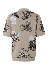 Polo en maille beige à manches courtes avec des motifs floraux abstraits noirs et blancs dispersés sur le tissu.