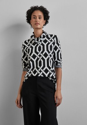 Zwart-wit geblokt top met een col, lange mouwen en hoge taille, gecombineerd met zwarte, hoog uitgesneden broek met een geometrisch ontwerp.