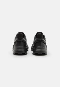 Černé sportovní boty s texturovaným svrškem, polstrovanou patou, robustní podrážkou a minimálním logem na boku.